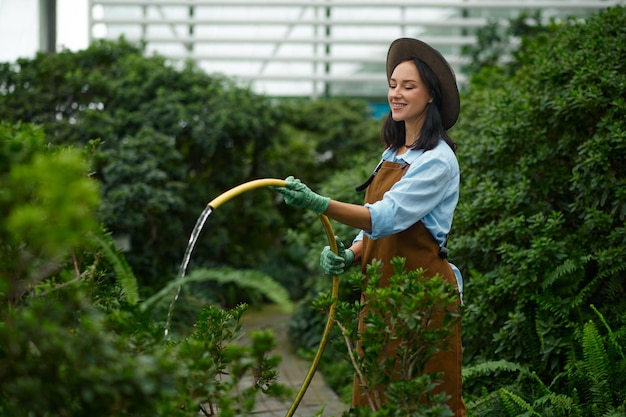 Jeune femme jardinier arrosant les plantes vertes du tuyau en serre