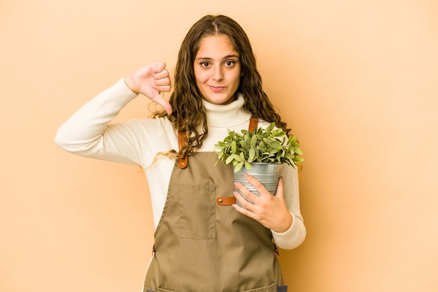 Jeune femme de jardinier caucasien tenant une plante isolée montrant un geste de dégoût, les pouces vers le bas. Concept de désaccord.