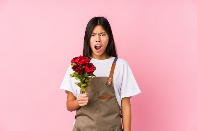 Jeune femme jardinier chinois tenant une rose isolée criant très en colère et agressif.