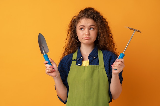 Jeune femme jardinier portant un tablier tenant des outils de jardinage sur fond jaune