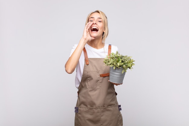 Jeune femme jardinier se sentir heureux, excité et positif, donnant un grand cri avec les mains à côté de la bouche, appelant