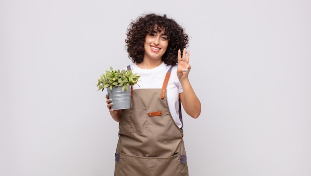 Jeune femme jardinier souriant et à la sympathique, montrant le numéro trois ou troisième avec la main en avant, compte à rebours