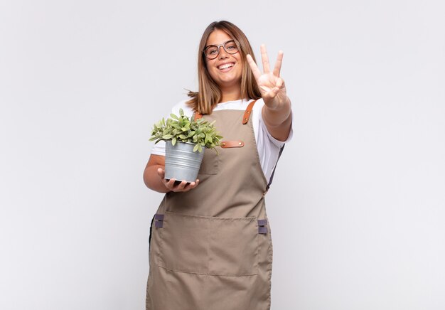 Jeune femme jardinier souriant et à la sympathique, montrant le numéro trois ou troisième avec la main en avant, compte à rebours