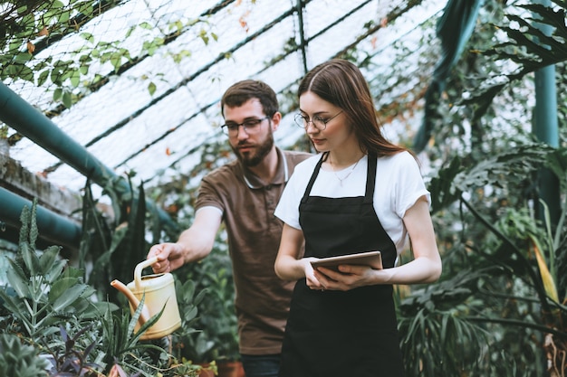 Jeune femme jardinier avec tablette numérique travaillant dans un centre de jardinage avec un collègue