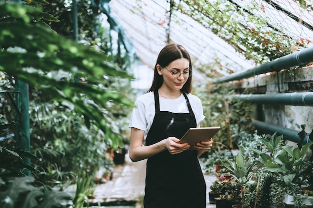 Jeune femme jardinier avec tablette numérique travaillant en serre