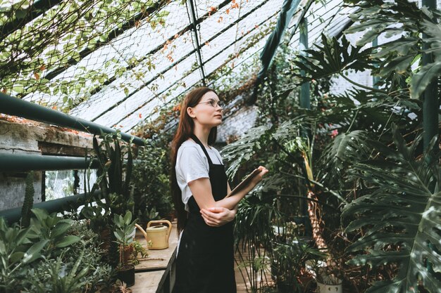 Jeune femme jardinier avec tablette numérique travaillant en serre