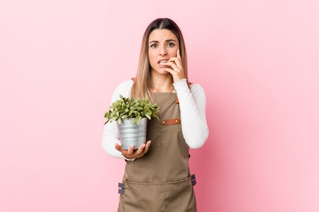 Jeune femme jardinier tenant une plante se rongeant les ongles, nerveuse et très anxieuse.