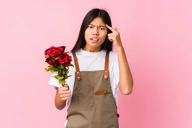 Jeune femme jardinier tenant une rose montrant un geste de déception avec l'index.