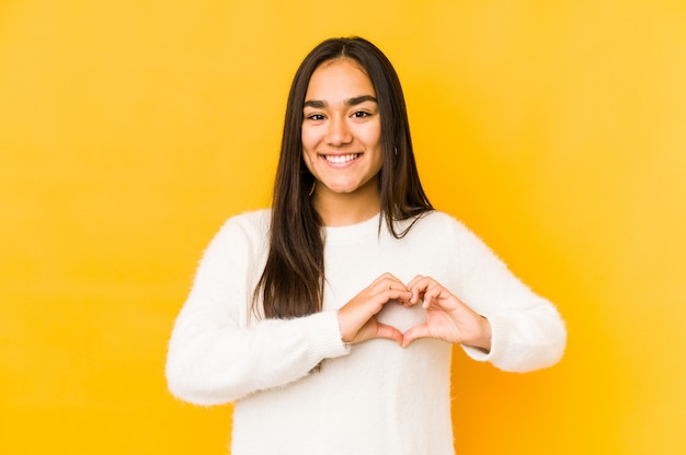 Jeune femme sur un jaune souriant et montrant une forme de coeur avec les mains.