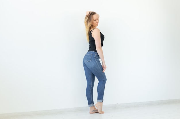 Jeune femme en jeans et chemise noire debout sur le mur blanc avec espace copie