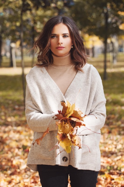 Jeune femme jetant des feuilles d'automne dans le parc d'automne à l'extérieur