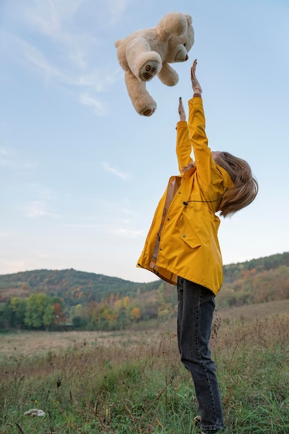 Jeune femme jeter un ours en peluche sur fond de collines ou de montagnes