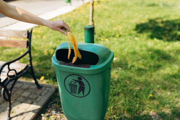 Une jeune femme jette une peau de banane dans une poubelle à l'extérieur en gros plan Recyclage des déchets