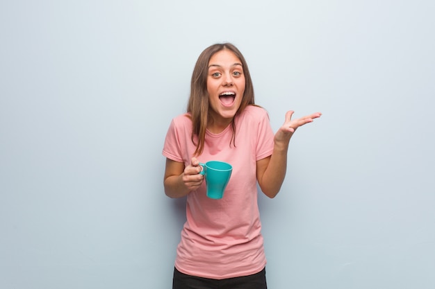 Jeune femme jolie caucasien célébrer une victoire ou le succès. Elle tient une tasse.