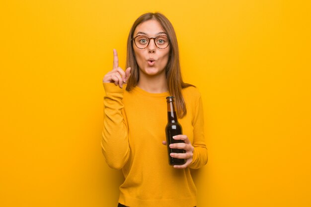 Jeune femme jolie caucasienne ayant une très bonne idée, concept de créativité. Elle tient une bière.