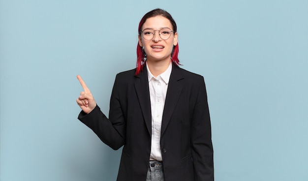 Jeune femme jolie cheveux roux souriant et à la recherche amicale, montrant le numéro un ou d'abord avec la main en avant