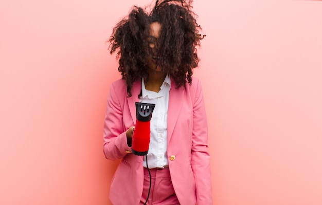 Jeune femme jolie noire avec un coiffeur contre le mur rose