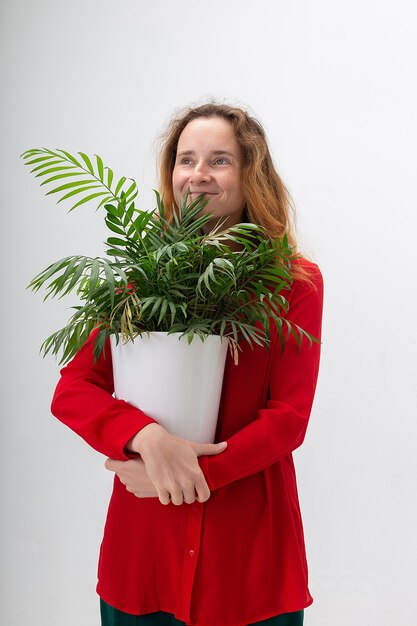 Jeune femme jolie souriante caucasienne tient une plante d'intérieur verte en pot dans ses bras