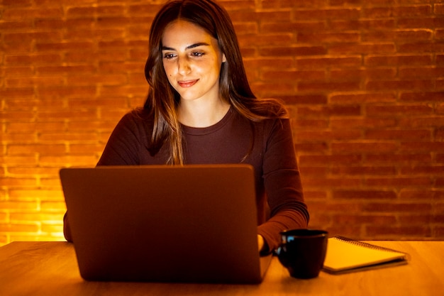 Une jeune femme jolie et souriante utilisant un ordinateur portable à la maison la nuit Une fille heureuse regardant l'ordinateur Des gens joyeux assis à un bureau dans le salon Concept de télétravail entrepreneurial et de personne travailleuse