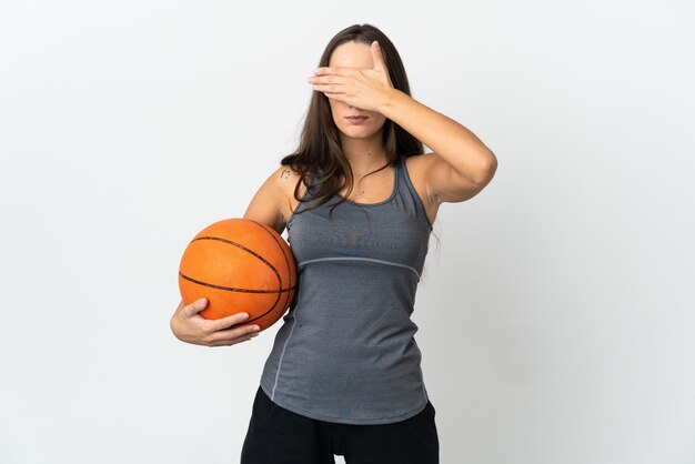 Jeune femme jouant au basket-ball sur fond blanc isolé couvrant les yeux par les mains. Je ne veux pas voir quelque chose