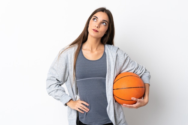 Jeune femme jouant au basket-ball isolé sur blanc pensant une idée tout en levant