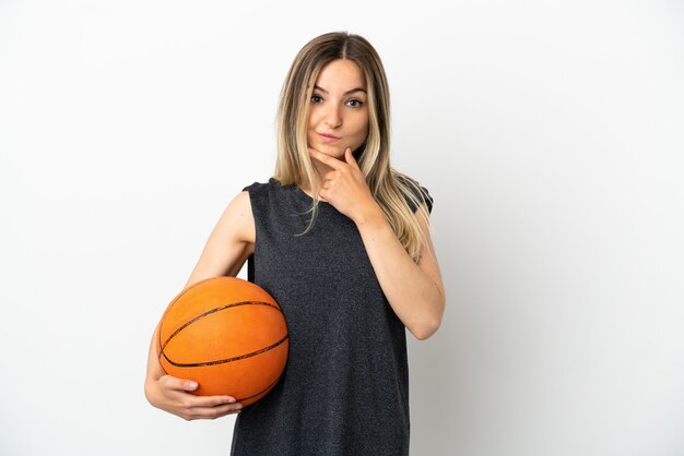 Jeune femme jouant au basket-ball sur mur blanc isolé pensant