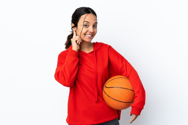 Jeune femme jouant au basket-ball sur mur blanc isolé en riant