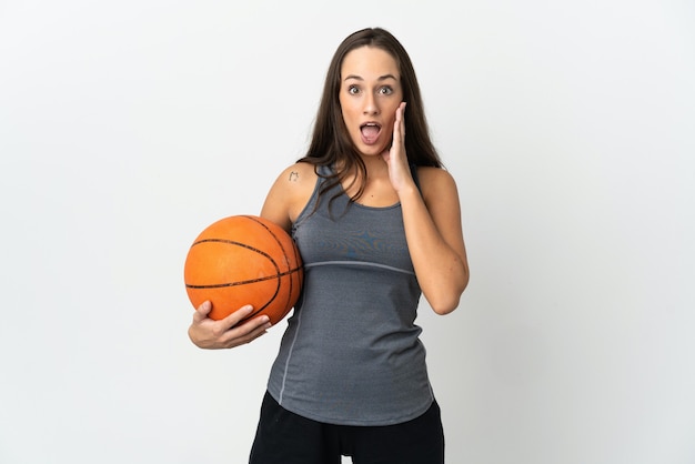 Jeune femme jouant au basket-ball sur un mur blanc isolé avec surprise et expression faciale choquée