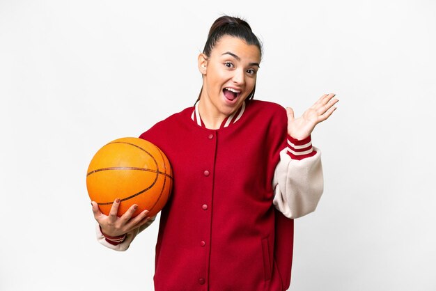 Jeune femme jouant au basket sur un fond blanc isolé avec une expression faciale choquée