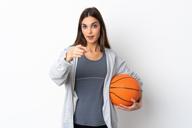 Jeune femme jouant au basket isolé sur blanc surpris et pointant vers l'avant