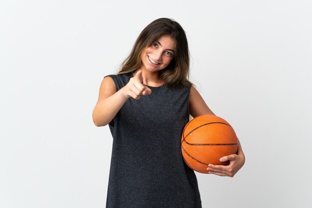 Jeune femme jouant au basket isolé sur fond blanc pointant vers l'avant avec une expression heureuse