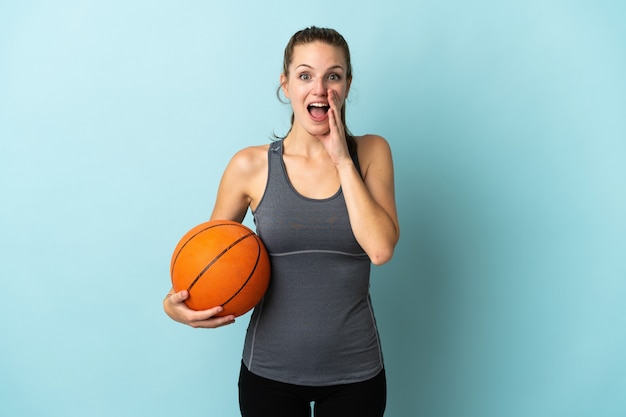 Jeune femme jouant au basket isolé sur fond bleu avec surprise et expression faciale choquée