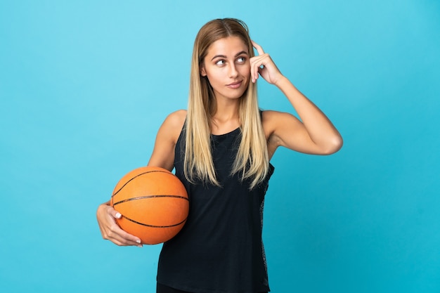 Jeune femme jouant au basket isolé sur un mur blanc ayant des doutes et de la pensée