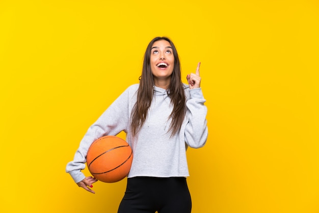 Jeune femme jouant au basketball isolé sur jaune pointant vers le haut une excellente idée