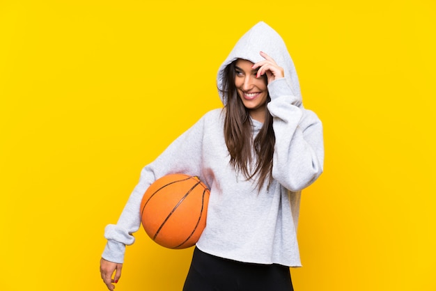 Jeune femme jouant au basketball sur un mur jaune isolé