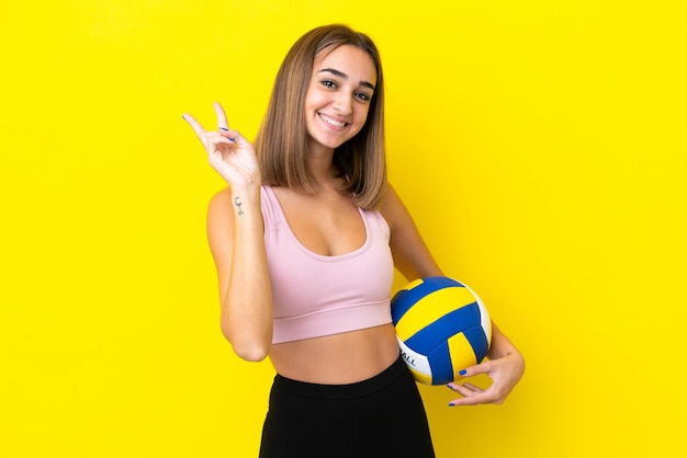 Jeune femme jouant au volley-ball isolé sur fond jaune souriant et montrant le signe de la victoire