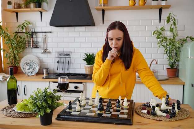 Jeune femme jouant aux échecs sur la table de la cuisine Femme joue dans un jeu de société logique avec elle-même dans la cuisine