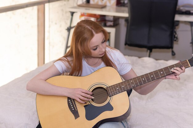 Jeune femme jouant de la guitare acoustique à la maison