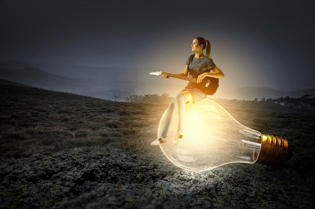 Photo jeune femme jouant de la guitare assis sur une ampoule. technique mixte