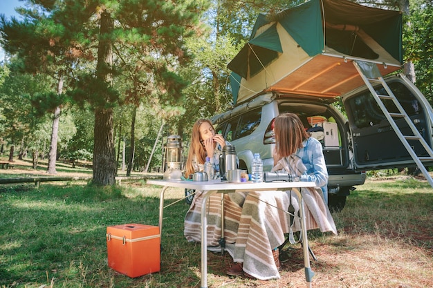 Jeune femme jouant de l'harmonica assis en camping avec son amie. Concept de temps libre et de plaisir.