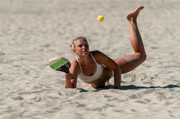 Une jeune femme joue au tennis sur la plage.