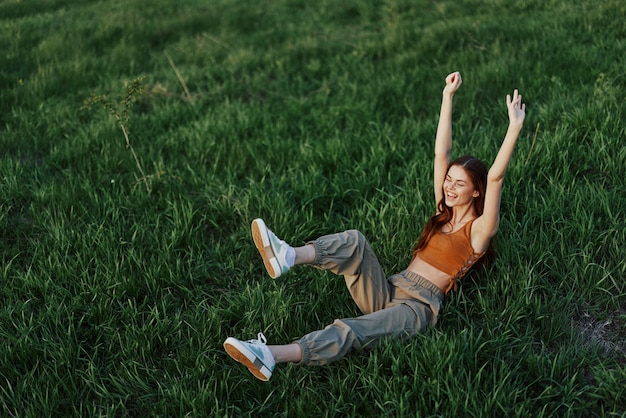 Une jeune femme joue dans le parc avec nous dans l'herbe et tombe au sol en souriant joyeusement au soleil Se reposer dans la nature en harmonie avec le corps