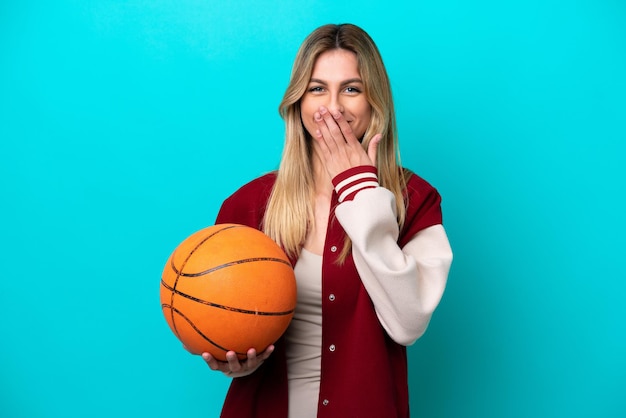 Jeune femme de joueur de basket-ball caucasien isolé sur fond bleu heureux et souriant couvrant la bouche avec la main