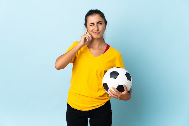 Jeune femme de joueur de football hispanique sur isolé sur bleu frustré et couvrant les oreilles