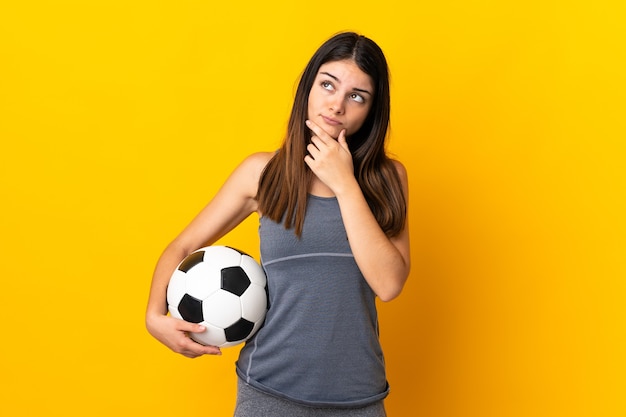 Jeune femme joueur de football isolé sur mur jaune ayant des doutes