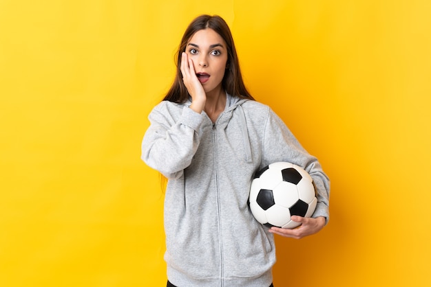 Jeune femme de joueur de football isolée sur fond jaune avec surprise et expression faciale choquée