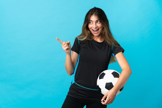 Jeune femme de joueur de football isolée sur le mur bleu pointant le doigt sur le côté et présentant un produit