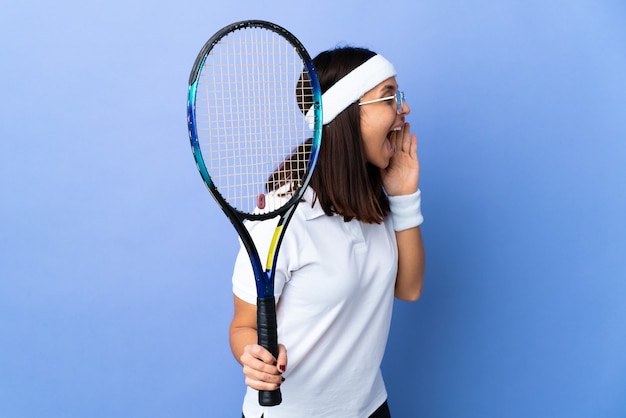 Jeune femme joueur de tennis sur fond isolé en criant avec la bouche grande ouverte sur le côté