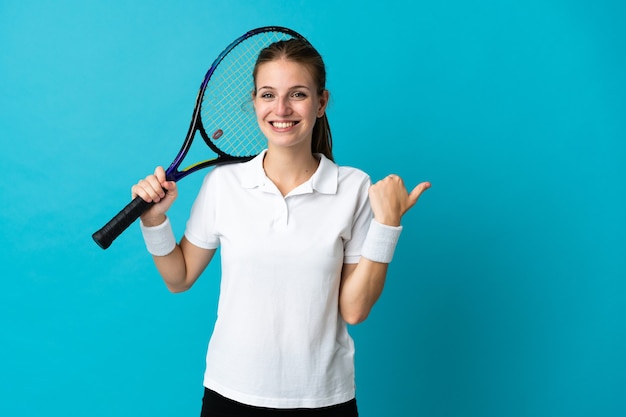 Jeune femme joueur de tennis isolé sur bleu pointant vers le côté pour présenter un produit