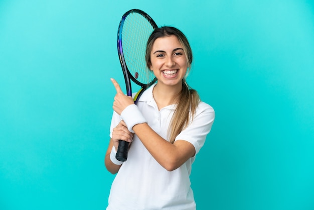 Jeune femme joueur de tennis isolé sur fond bleu pointant vers le côté pour présenter un produit